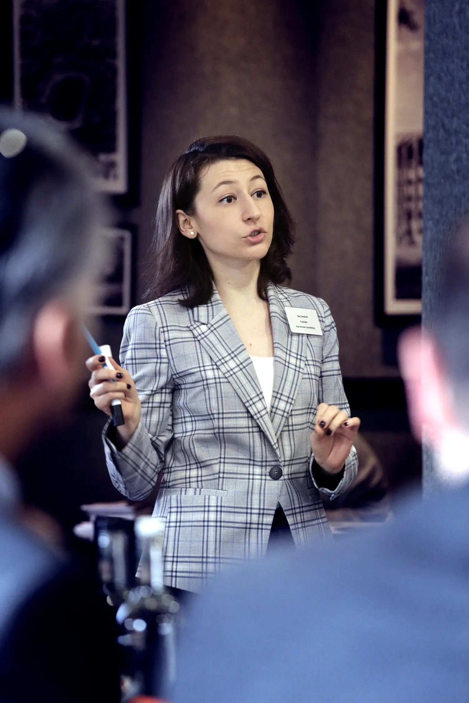 Woman in plaid blazer presenting to colleagues during meeting